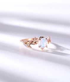 a white opal ring with leaves on the side and an opal stone in the middle