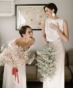 two women standing next to each other in front of a couch with flowers on it