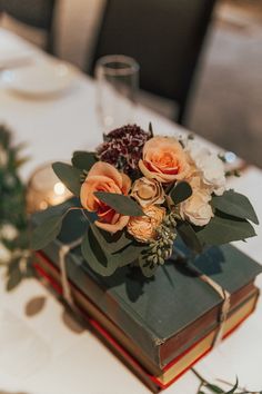 an arrangement of flowers is sitting on top of two books at the head table for a wedding reception