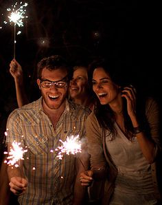 a group of people standing next to each other holding sparklers in their hands and laughing