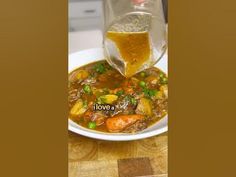 a bowl of stew with carrots and peas is being poured into a glass pitcher