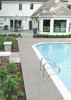 an empty swimming pool in front of a white house with landscaping around it and steps leading up to the pool