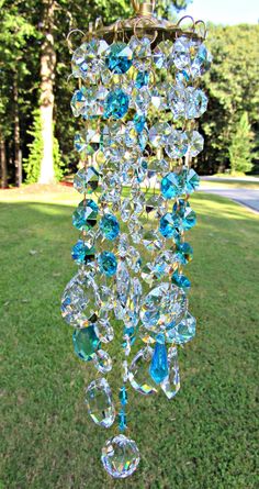 a blue glass chandelier hanging from a chain in the grass with trees in the background