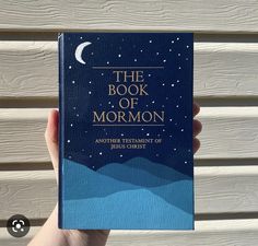 the book of mormon is held up in front of a white wall with blue mountains