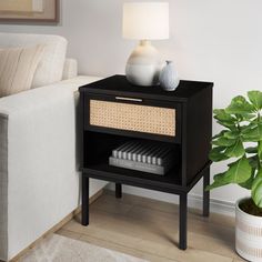 a living room with a white couch and a black end table next to a plant