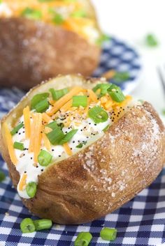 two baked potatoes with cheese and green onions on a blue checkered cloth next to a fork