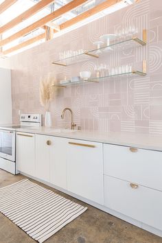 a kitchen with white cabinets and pink wallpaper on the walls, along with an area rug