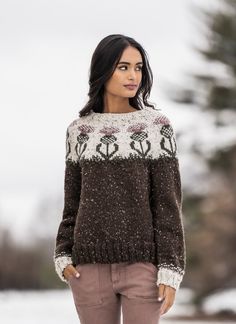 a woman standing in the snow wearing a brown and white sweater with flowers on it