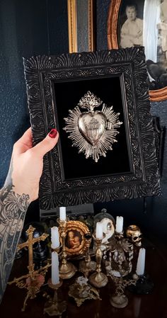 a person holding up a framed artwork with candles on the table in front of it