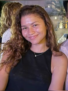 a woman with long curly hair smiling at the camera while standing next to a man