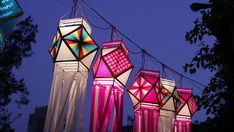 colorful lights hanging from wires in front of trees and buildings at night with blue sky