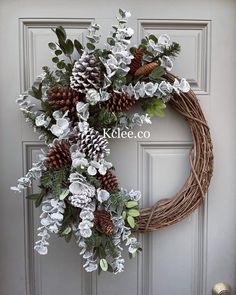 a wreath with white flowers and pine cones is hanging on the front door to welcome guests