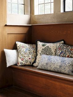 a wooden bench with pillows on it in front of two windows and a window sill