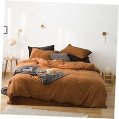 a bed with brown sheets and pillows in a white room next to a wooden floor