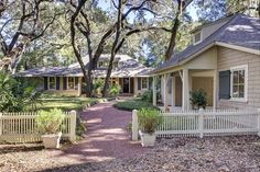 a white picket fence in front of a house with trees and bushes around it on a sunny day