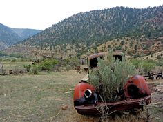 an old rusted out car sitting in the middle of a field with mountains in the background