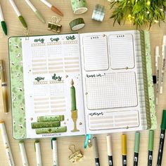 an open planner book surrounded by pens, markers and pencils on a wooden table