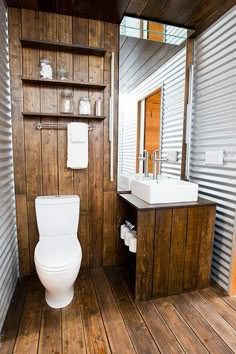 a white toilet sitting inside of a bathroom next to a wooden counter and sink under a mirror