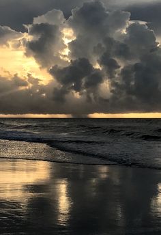 the sun is setting over the ocean with clouds in the sky and water on the beach