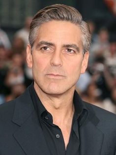 a man with grey hair and black shirt standing in front of a group of people