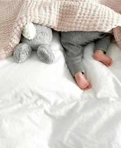 a small child laying under a blanket on top of a white bed covered in blankets