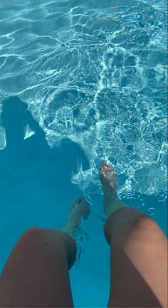 a person standing in the water with their feet on the edge of a swimming pool