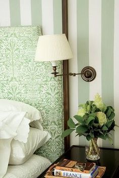 a lamp is next to a bed with green and white striped wallpaper on it