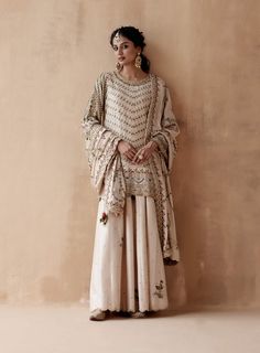 Editor's Note Introducing an exquisite ivory kurta adorned with intricate floral thread embroidery, elegantly highlighted with various embellishments. This captivating ensemble is paired with a stunning sharara and a heavily embroidered dupatta, creating a luxurious and regal look perfect for grand occasions or festive celebrations. The combination of the intricate embroidery, embellishments, and the richness of the dupatta adds an opulent touch, making this outfit a statement of classic eleganc Floral Thread Embroidery, Embroidery Embellishments, Embroidered Dupatta, Sharara Set, Thread Embroidery, Intricate Embroidery, Floral Embroidery, Embellishments, Thread