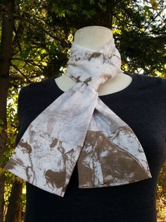 a white and brown scarf on top of a mannequin's head with trees in the background