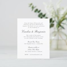 a white wedding card sitting on top of a table next to a vase with flowers