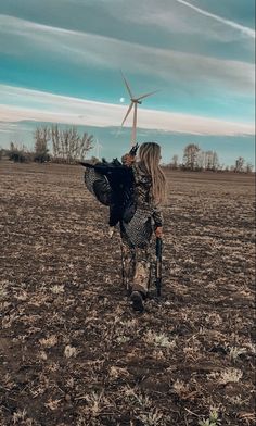 a woman walking across a field with a wind turbine in the background