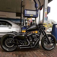 a black motorcycle is parked in front of a gas station with a silver car behind it