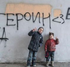 two young boys standing next to each other in front of graffiti written on the wall