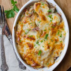 a casserole dish with meat and cheese on a wooden table next to a fork