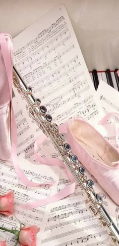 a pink ballet shoe sitting on top of sheet music next to roses and a flute