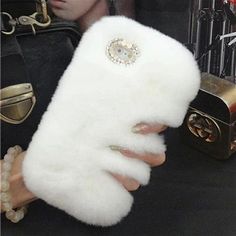 a woman's hand holding a white fur phone case in front of a mannequin