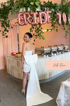 a woman in a white dress standing next to a table with food and balloons hanging from the ceiling