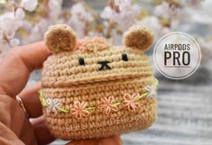 a hand holding a small crocheted bear with flowers on it's face