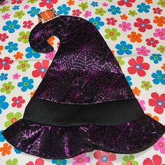 a purple witch hat sitting on top of a flower covered tablecloth with black ribbon