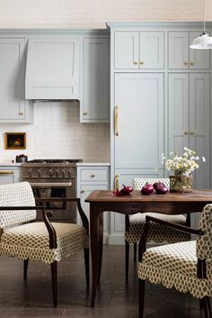 a kitchen with blue cabinets and white walls, two chairs at a table in front of an oven