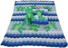 a crocheted blanket with green frogs on it and two pillows in the middle