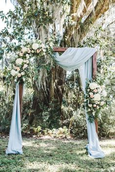 an outdoor wedding ceremony with blue drapes and white flowers on the arch, surrounded by trees