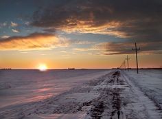 the sun is setting over an empty field with snow and power lines in the foreground