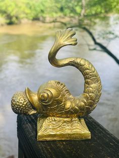 a gold fish statue sitting on top of a wooden fence next to a body of water