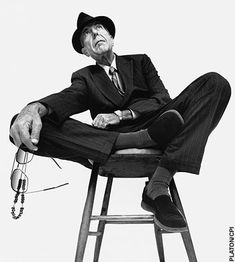 a man sitting on top of a stool wearing a suit and hat with his legs crossed