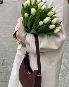 a woman holding a brown purse with white tulips in her hand on the street