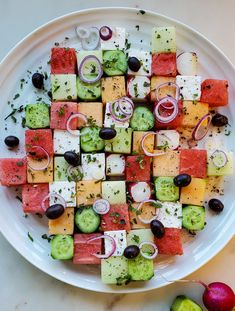 a white plate topped with cucumbers, tomatoes and olives next to other vegetables