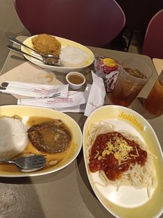 two plates of food on a table with some drinks and spoons next to it