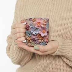 a woman holding a coffee mug with flowers on it in her left hand while wearing a beige sweater