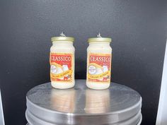 two jars of cheese sitting on top of a silver plate next to each other in front of a black wall